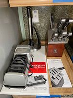 Photo showing Chefs Choice Trizor XV electric knife sharpener, Henckels wooden knife block with knives, and stainless steel paper towel holder on countertop.