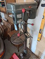 Front side view of the full Duracraft floor drill press showing the metal base, column, worktable, and red-handled levers.