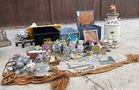 Wide view of garden decor collection laid out including gnomes, figurines, storage boxes, plaques, and milk jug.