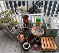 Overview of assortment showing plant stand, pots, wagon, toolbox, statuaries, and gardening supplies arranged on porch