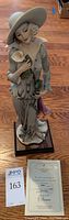 Full view of sculpture on wood base with certificate of authenticity and lot number card