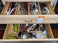 Photo of two open wooden drawers filled with assorted kitchen utensils and serving tools. Items include graters, peelers, spatulas, tongs, whisks, can openers, and measuring cups.