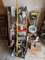 Full view of stacked painting tools and supplies with baskets and boxes containing various brushes, trowels, rollers, sandpaper rolls and buckets.