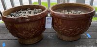 Photo showing the pair of large glazed ceramic pots filled with stones, placed outdoors with greenery background.