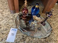 Lot of various decorative perfume bottles, three silver-tone rhinestone hair combs, and an oval mirrored tray displayed together on a stone countertop.