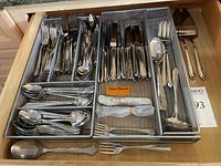 Top view of the organized flatware in metal mesh trays showing knives, forks, spoons, and serving pieces.