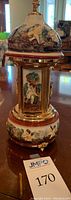 Front view of porcelain dispenser music box showing painted dome with cherubs and metal base