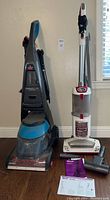 Photo showing both Shark Navigator Lift-Away vacuum and Bissell Deep Clean ProHeat 2X carpet cleaner together, along with accessories and manuals on floor.