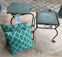 Photo shows two wrought iron side tables, one with a square slate top and two turquoise square accent pillows with white geometric pattern on the ground.