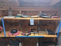 Photo of small gardening tools including hand rakes, trowels, hose adapters and cultivators arranged on a wooden shelf.