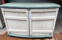 Full front view of the Suncast storage bin showing beige plastic body, green lid, double doors with latch and padlock location.