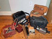 Wide photo showing the collection of vintage cameras, camcorder, tripod with case, Binolux optics, and leather and fabric cases.