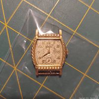 Front view of antique Gruen watch showing detailed patterned dial, Arabic numerals, and gold-tone case with beaded and rope accents.