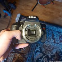 Front view of Canon EOS Rebel T3i DSLR camera body held in hand, showing the lens mount without lens attached.