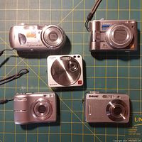 Top front view of five digital cameras showing Sony Cyber-shot DSC-P7, Panasonic Lumix, Olympus FE-170, Sony Cyber-shot DSC-P32, and Fujifilm FinePix Z1