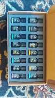 Photo of open box containing 12 small glass bottles of essential oils with black labels and various colored text, arranged in two rows of six.