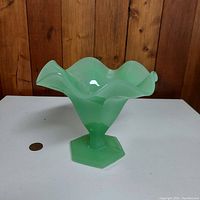 Front angle showing the ruffled edge, hexagonal pedestal base, and translucent light green jadeite glass material with a smooth glossy surface.