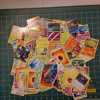 Spread of assorted Pokemon cards on a grid cutting mat showing different types, colors, and holographic finishes.