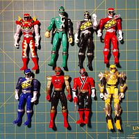 Front view of all 8 Power Rangers action figures arranged in two rows on a grid surface showing colors and details.
