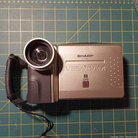 Front view of Sharp ViewCam VL-E380 camcorder showing lens, 8mm recording label, and hand strap.