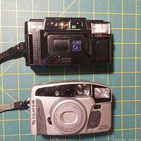 Front of Ricoh FF-9 and Fujifilm Discovery 290S 27mm film cameras showing lens, flash, and controls.