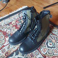 Pair of Urban Outfitters combat boots placed on a patterned rug. Shows front and side views with visible laces, zippers, and buckles.