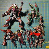 Top-down photo of six Spawn action figures displayed on grid background showing size and condition