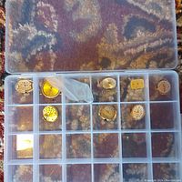 Plastic organizer box with 9 compartments containing assorted watch movements and parts. Some movements have gold-tone dials and others silver-tone. One movement contained in small plastic bag.