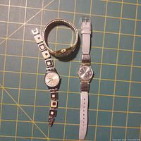 Two women's Swatch watches: one with a gold-tone expandable band, the other with a white leather strap and silver-tone watch face.