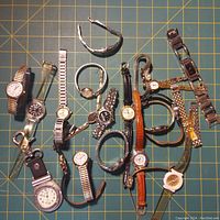 Full lot of 13 women's watches laid flat on green cutting mat showing variety of styles and bands