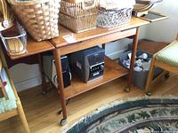 Front and side view of wooden bar cart with drop leaves folded down, baskets on top and speakers on lower shelf
