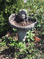 Full view of the concrete angel birdbath located outdoors among plants and leaves.