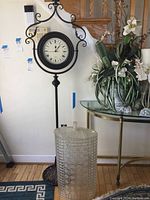 Overall view of the black metal standing clock next to the vintage plastic hamper with lid