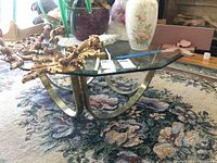 Full view of the glass top coffee table showing clear beveled edge glass and brass toned metal curved legs with decorative items on top (not included).