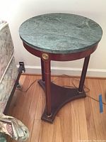 Round end table with green stone top, three wooden legs, and triangular wooden base with gold-tone accents on legs.