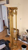 Full view of the tall brass colored metal floor lamp, showing its classical design, four vertical pillars, and frosted glass shade.