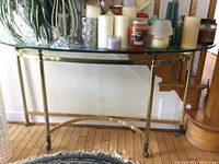 Full view of foyer table showing glass top and brass-toned base with curved support bar and slender legs.