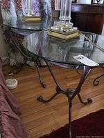 Two matching round glass top tables with metal bases, positioned side by side with glass tops clear and bases showing elegant curled legs.