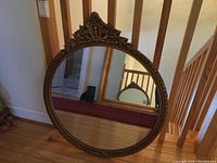Full view of the round framed mirror leaning against a staircase wall, showing the whole mirror and frame.