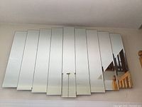 Front view of nine vertical mirror panels arranged side by side, mounted on wall.