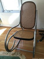 Front angle view of the chrome and cane vintage rocking chair showing curved chrome rockers and woven cane seat and backrest.