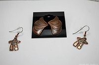Photo showing two pairs of copper earrings, wing-shaped and abstract figure-shaped, displayed on and around a black card.