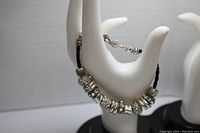 View showing multiple silver-tone beads with clear rhinestones on braided black leather bracelet worn over a hand display.