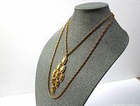Front angle of gold tone double chain necklace with long 28" chain and shorter 18" chain, featuring a large connected floral pendant.