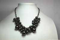 Full view of the necklace displayed on a white mannequin bust showing clustered black metal beads along the chain.