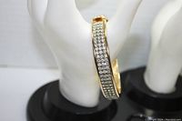 Front view of gold tone bracelet encrusted with clear rhinestones on multi-row claw setting, displayed on hand mannequin.