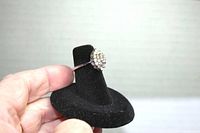 Costume ring shown from side angle on black ring display, held by hand. Shows the ring's cluster setting with multiple small stones and thin band.