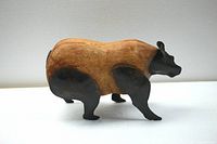 Side view of a hand-carved wooden animal figure with metal head, legs, and tail showing profile and details.