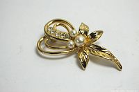 Clear overall view of the gold tone flower-shaped brooch with faux pearl centers and rhinestone detail on ribbon element, showing front face.
