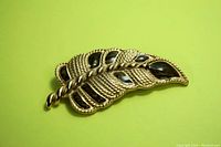 Front view of gold-tone brooch shaped as a feather or leaf with enamel sections on a pale green background.